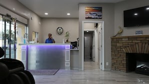 A reception area with a counter, a television mounted on the wall, a fireplace, and a painting above the fireplace. - Heritage Inn (Daytona Beach)