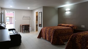 A hotel room with two beds, a desk, a chair, and a view of the outside. - Heritage Inn (Daytona Beach)
