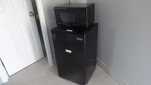 A compact black refrigerator and microwave unit in a corner of a room with light grey flooring and a white door. - Heritage Inn (Daytona Beach)