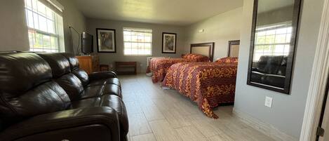A spacious room with a leather sofa, two beds with patterned bedding, a large mirror, and artwork on the walls.