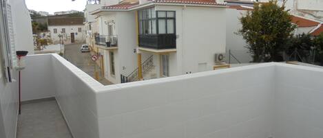 A balcony with a view of a residential street, white tiled walls, and a door with a broom leaning against it.
