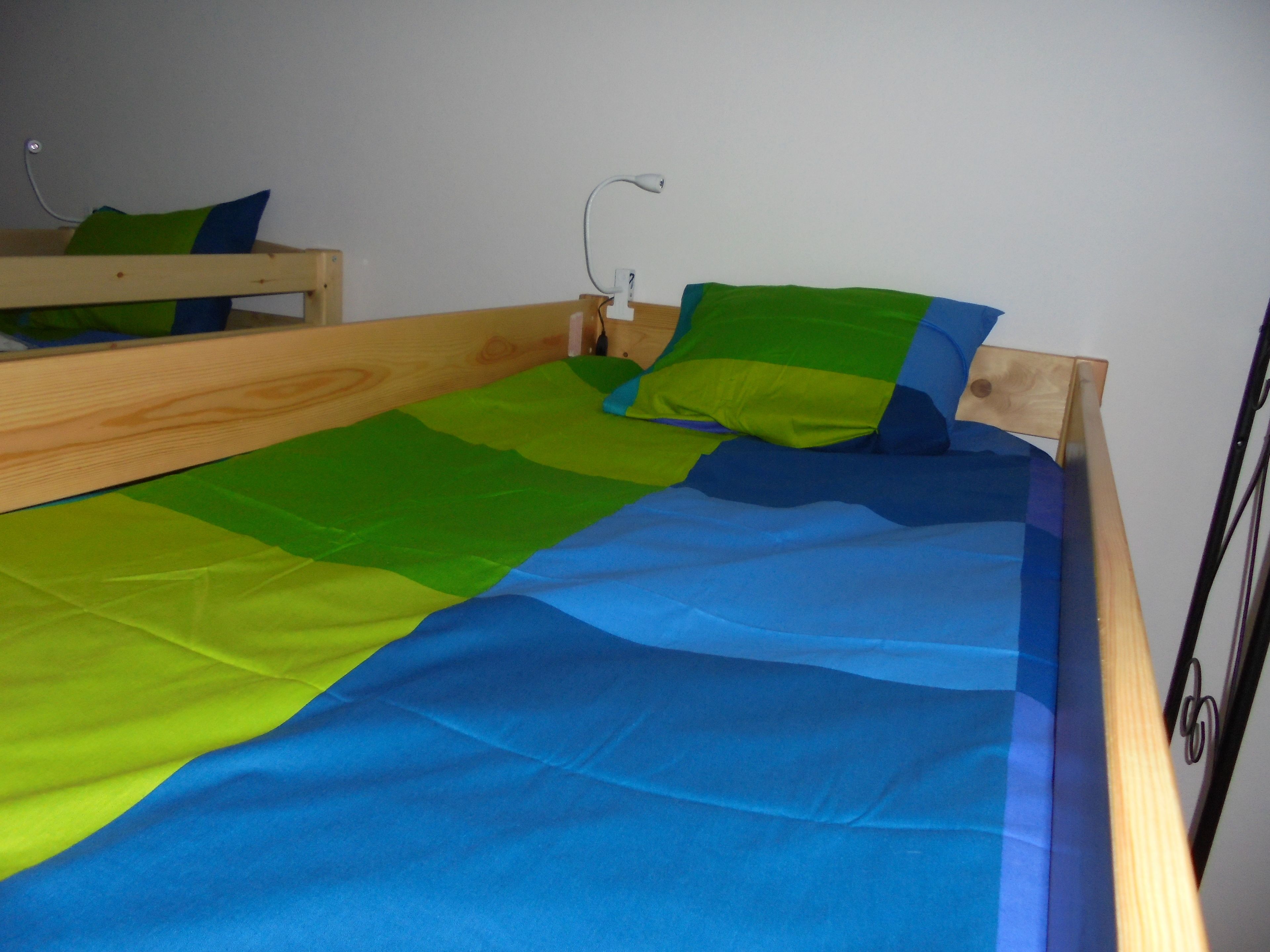 Una cama de madera individual con colcha azul y verde.
