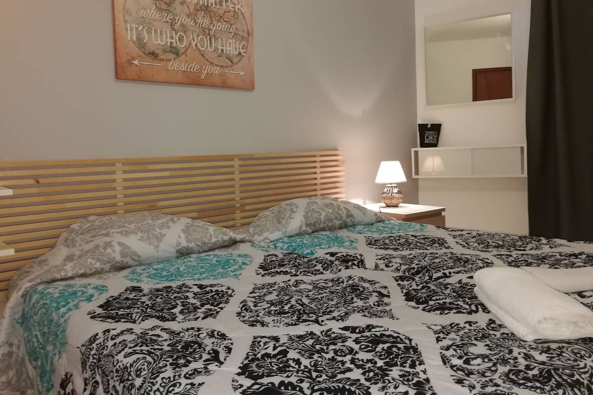 A neatly made bed with patterned bedding, a wooden headboard, a bedside lamp, and a motivational quote on the wall.