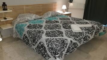 Un lit bien fait, recouvert d’une couvre-lit à motifs, une table de chevet avec une lampe et une étagère fixée au mur.