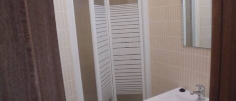 Un baño con ducha, lavamanos y espejo.