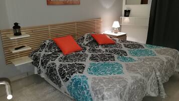 Ein Schlafzimmer mit einem Bett, zwei roten Kissen, einem Nachttisch mit Lampe, einer Wanduhr und einem motivierenden Zitat.