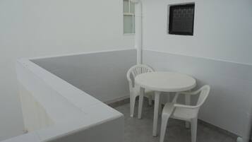 Un pequeño balcón cerrado con una bañera blanca, dos sillas de plástico blancas y una mesa redonda pequeña.