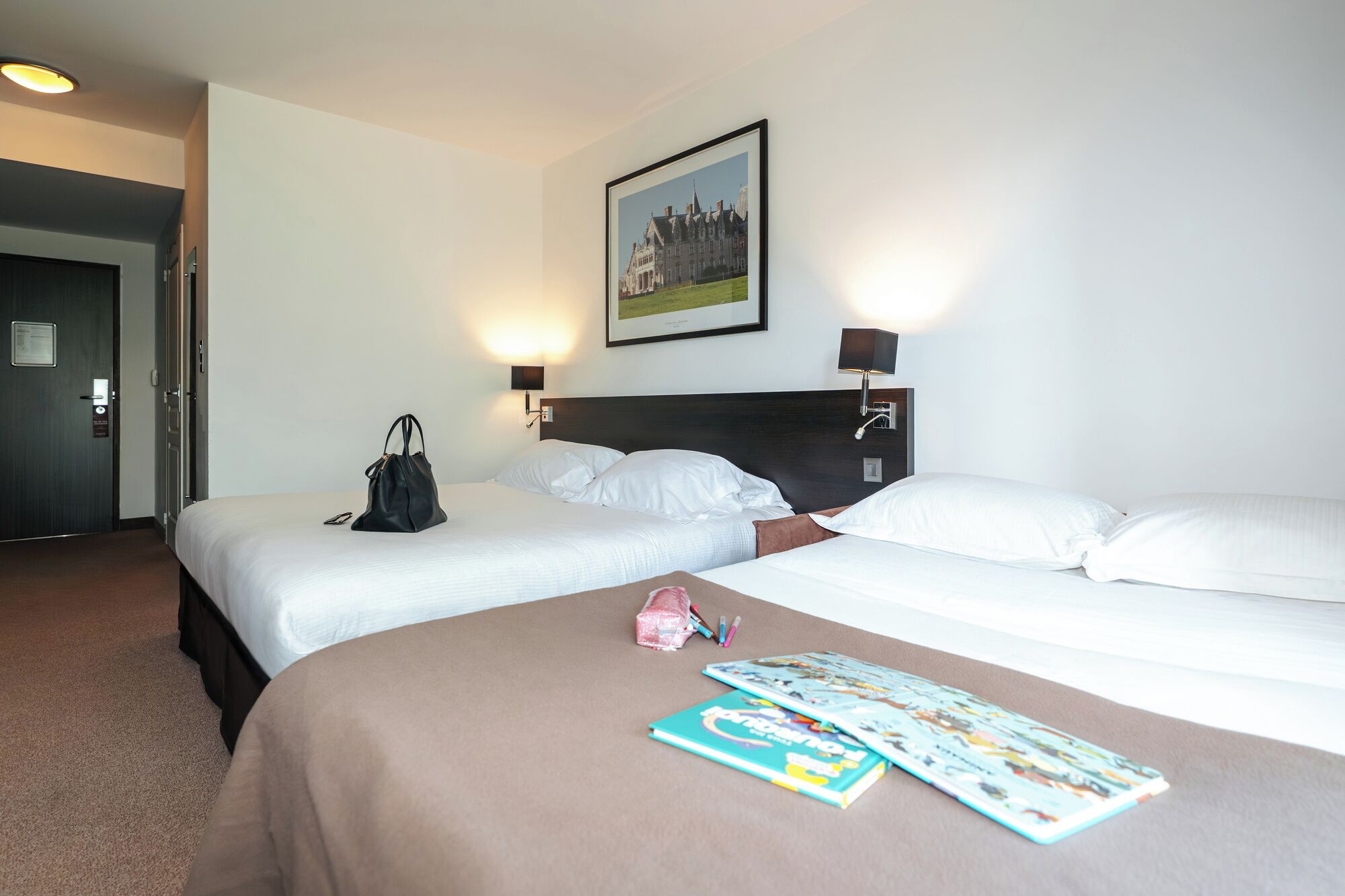 A hotel room with two beds, a framed picture on the wall, and a handbag on one bed.