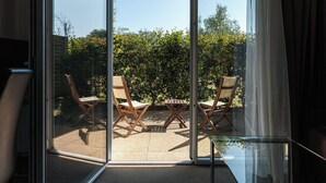 Una habitación con una puerta corrediza de vidrio que da a un espacio exterior con dos sillas de madera y una mesita.