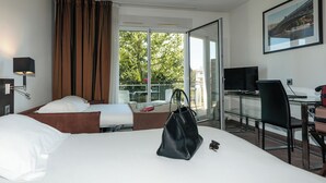 Habitación de hotel con dos camas, un escritorio con una computadora, una silla y un ventanal con vistas a zonas verdes.