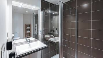Une salle de bain moderne avec deux vasques, une douche en verre et des murs recouverts de carreaux de couleur sombre.