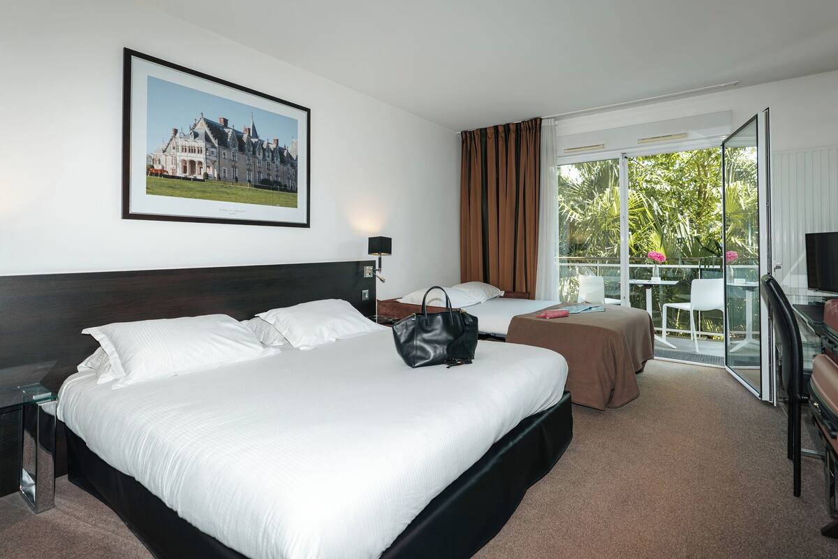 Habitación de hotel con una cama grande, un escritorio, una silla, televisión y balcón con vistas a zonas verdes.