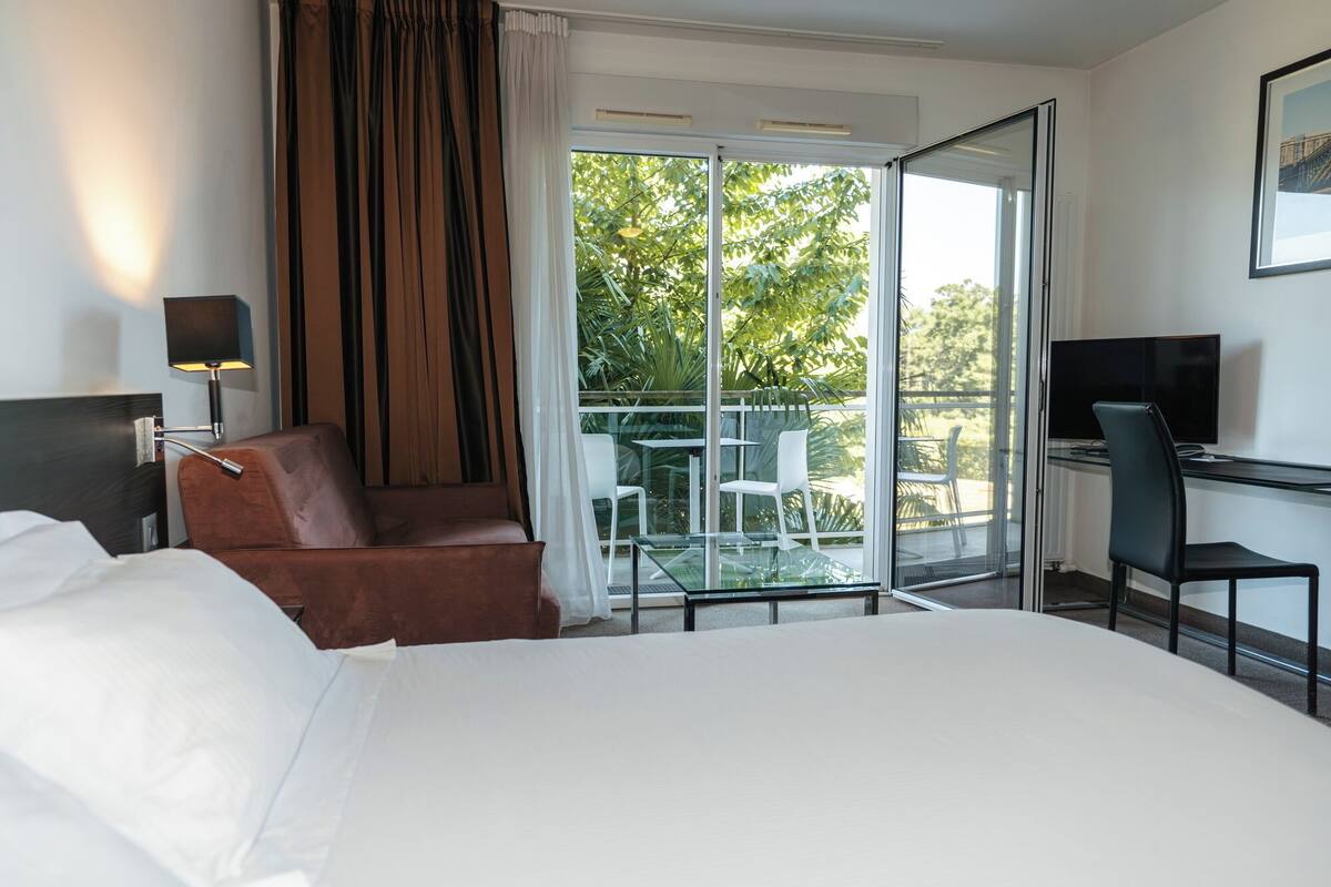 Habitación de hotel con cama, escritorio con computadora, silla, sofá y balcón con puerta de cristal.