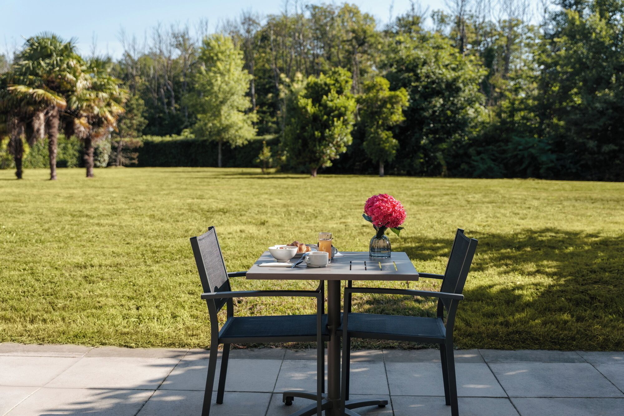 Une table dressée à l’extérieur, avec des chaises, un vase de fleurs et un repas.