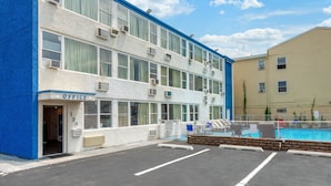 Un immeuble de deux étages, avec une enseigne « Bureau » au rez-de-chaussée, une piscine entourée d  ’une clôture et un parking.
