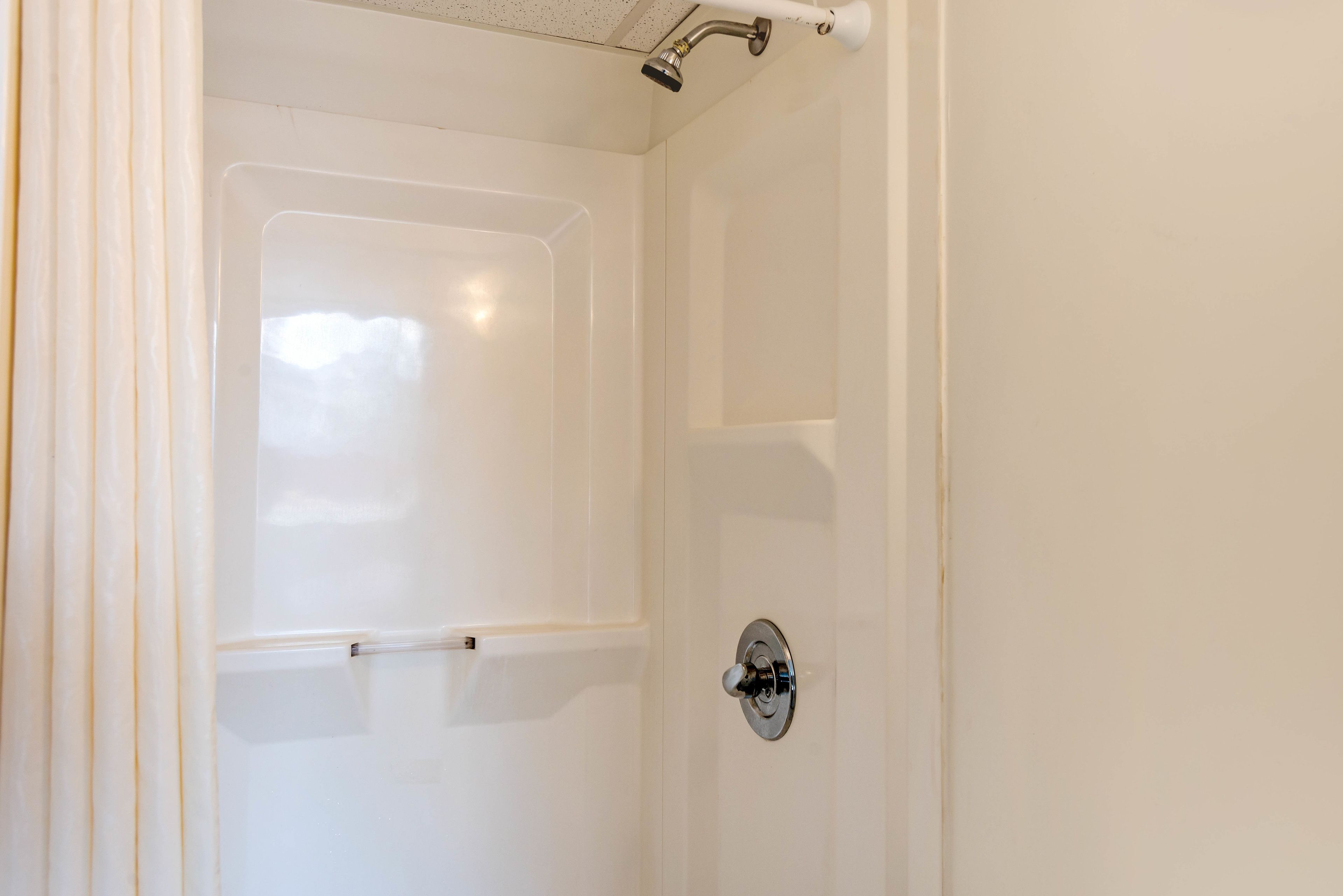 A white shower with a handheld showerhead and a wall-mounted control.