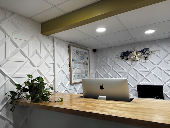 Un mostrador de recepción con una computadora portátil, un collage de fotos enmarcadas y una planta en maceta.