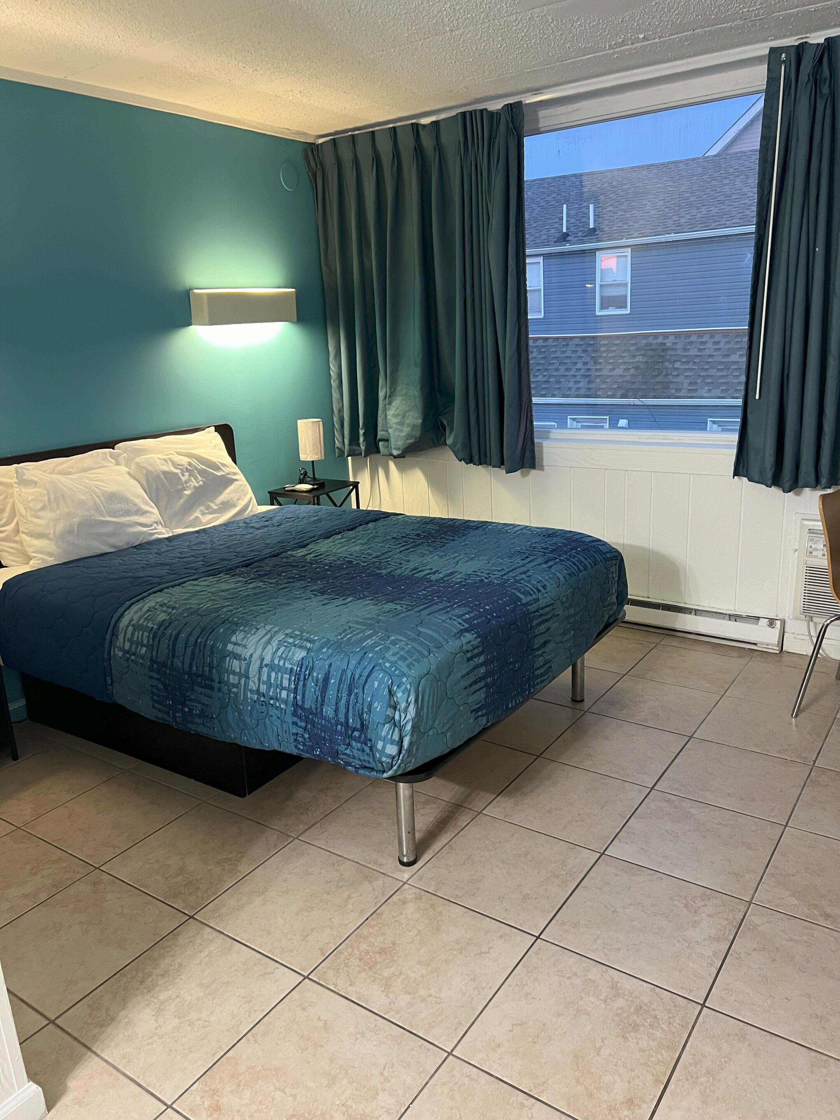 A bedroom with a bed, a nightstand, a lamp, and a window with curtains.