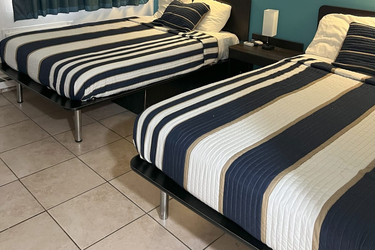 Ein Hotelzimmer mit zwei Betten, türkisfarbenen Wänden und einem Fenster mit Vorhängen.