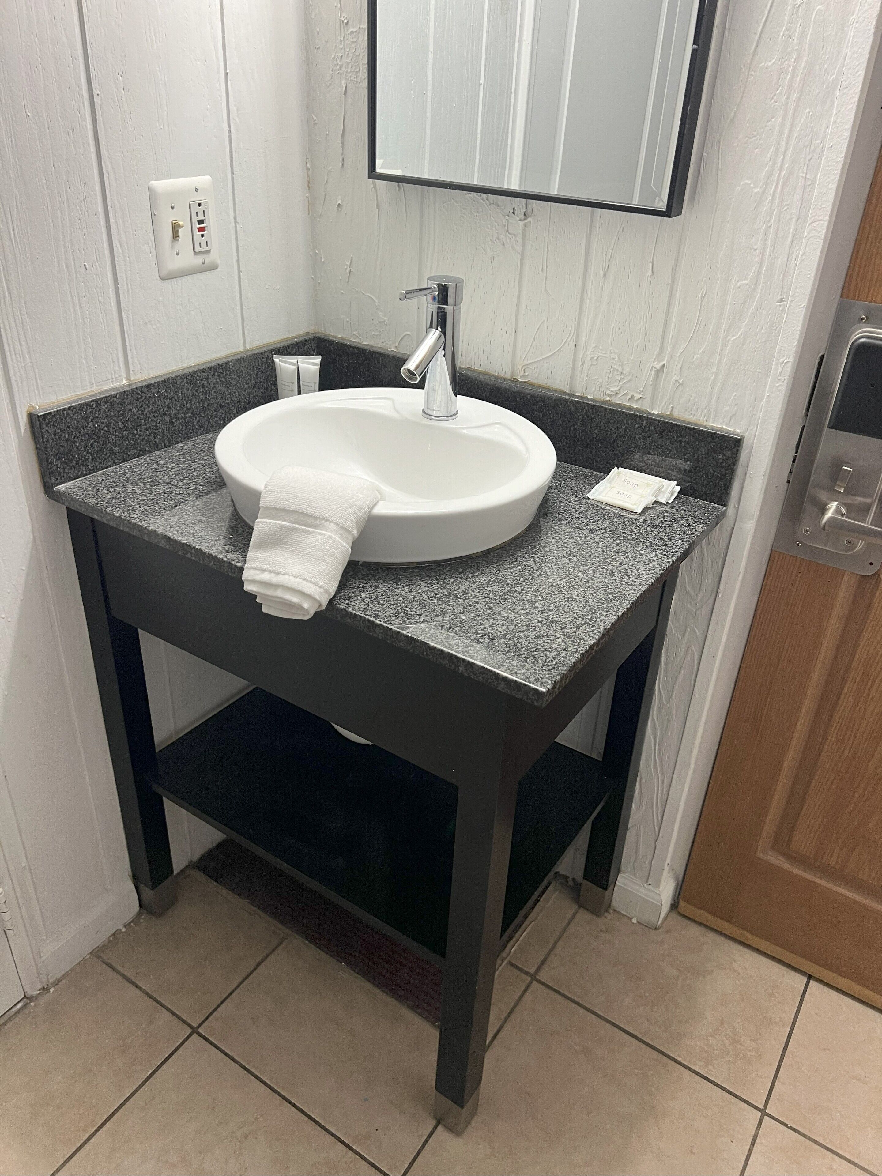 A bathroom with a white sink, dark countertop, and a mirror above it.