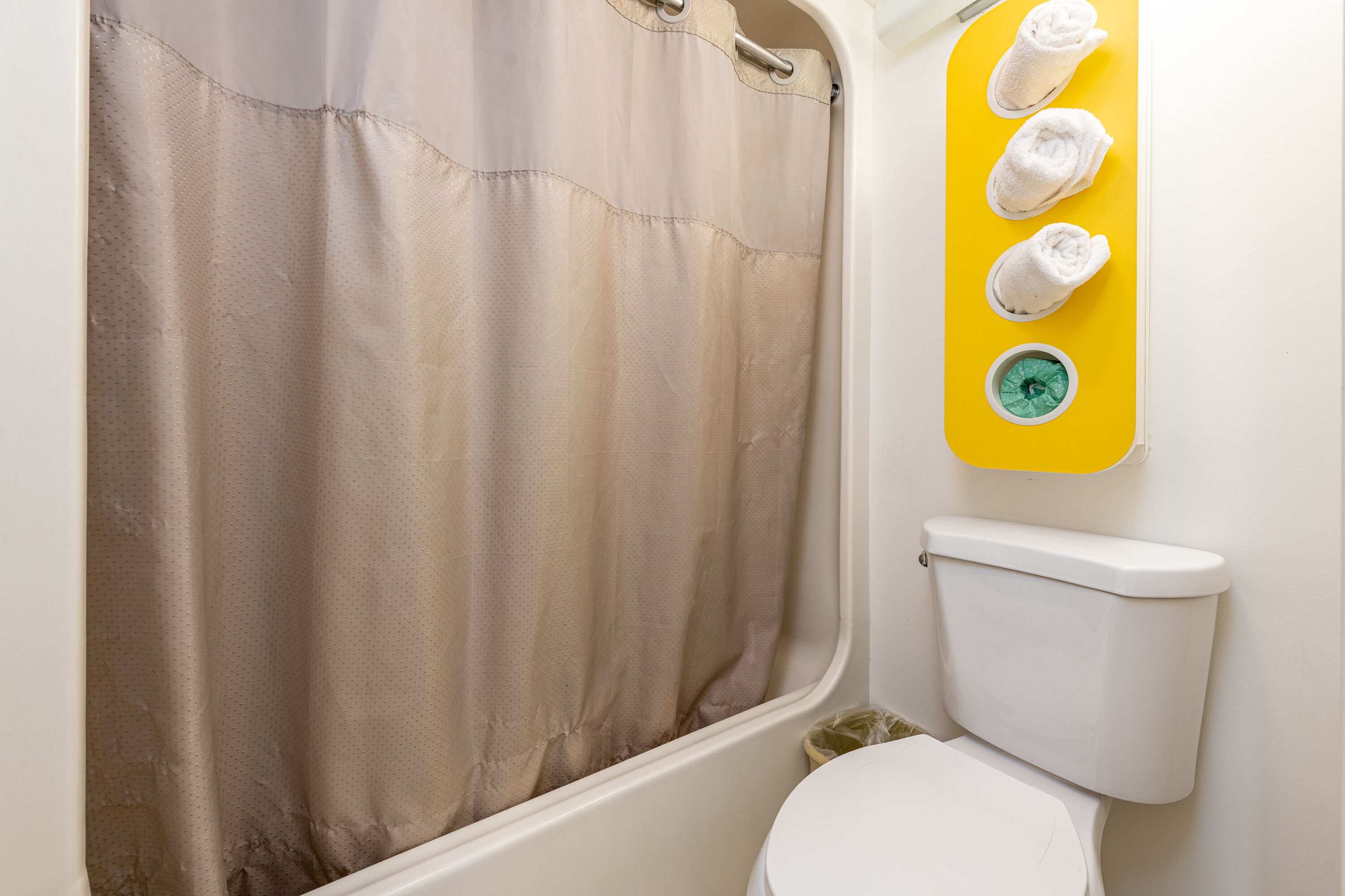 Une salle de bain avec un rideau de douche, des toilettes et un porte-serviettes avec des serviettes.