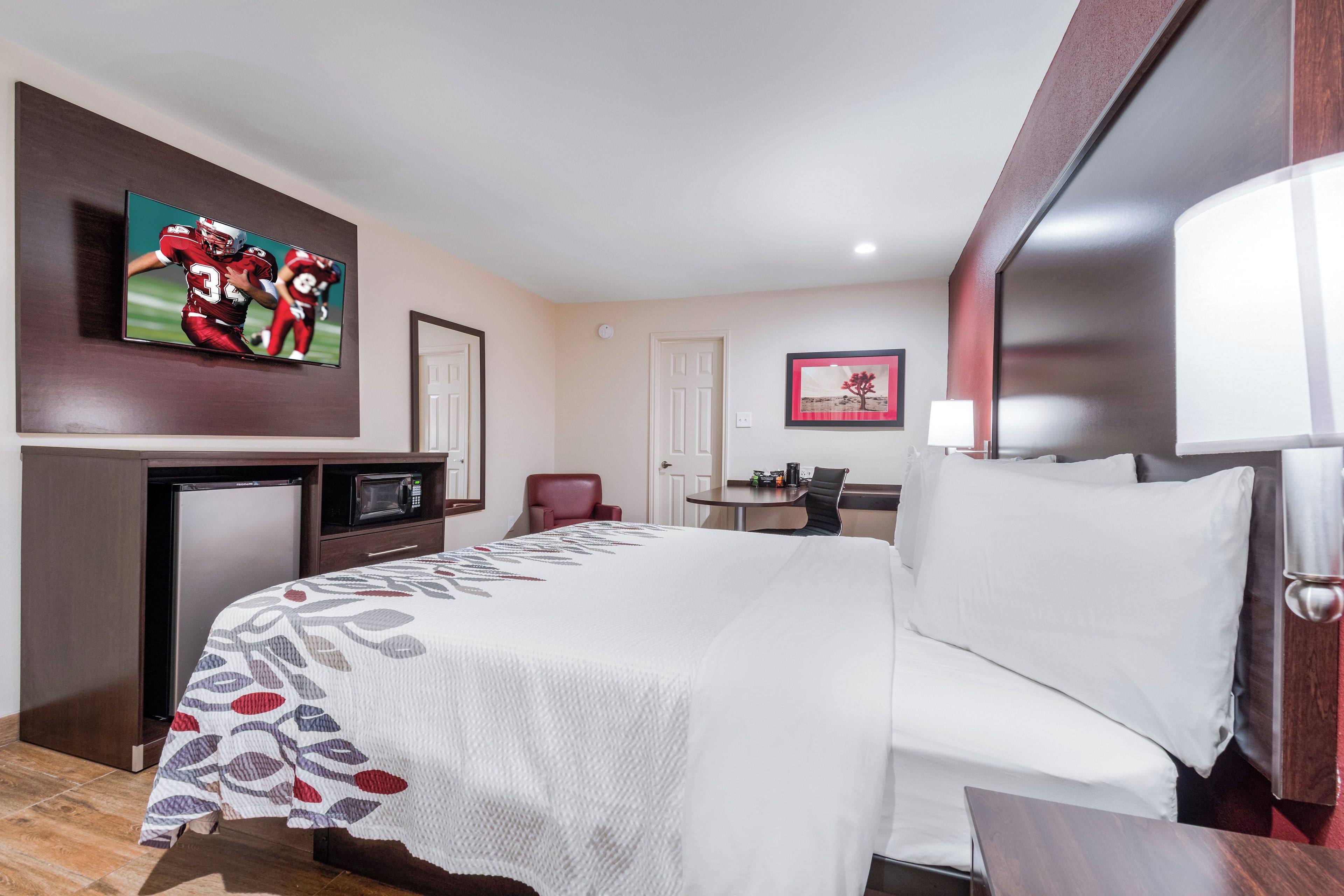 A hotel room with a bed, a desk, a television, and a small kitchenette.