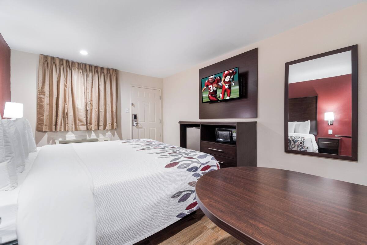 A hotel room with a large bed, a flat-screen TV mounted on the wall, a wooden side table, and a mirror.