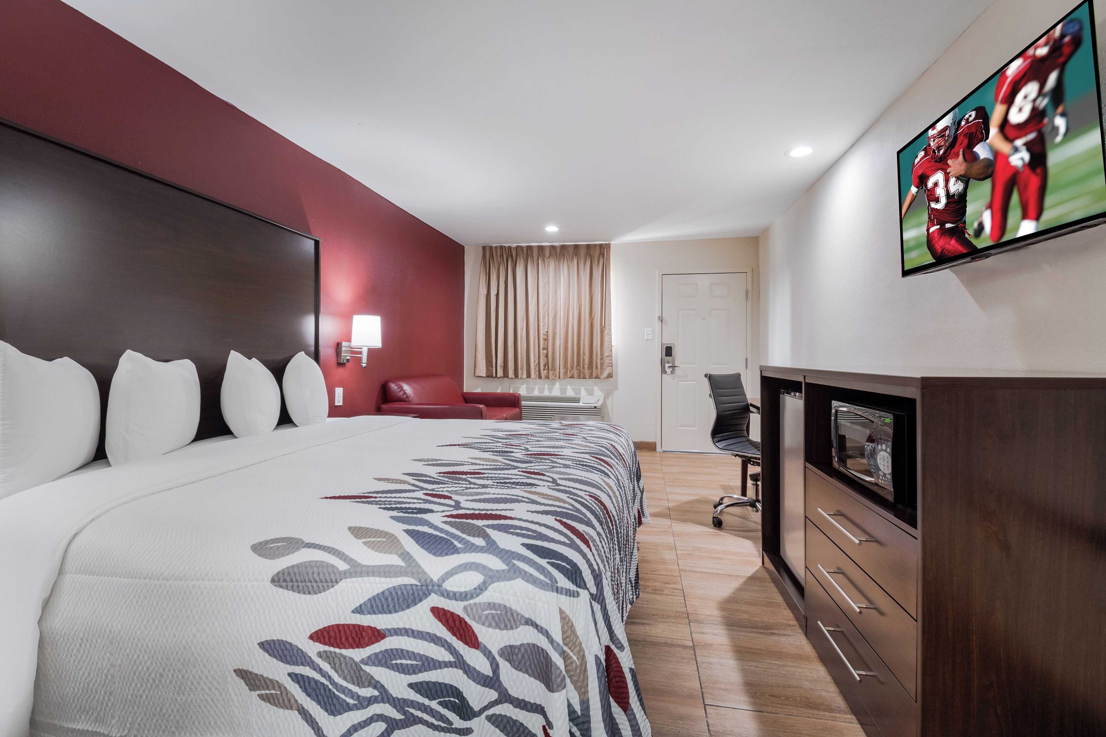 Una habitación de hotel con una cama grande, televisión, escritorio y una silla.