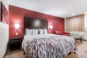 Una habitación de hotel con una cama grande, una silla roja, un escritorio y una ventana con cortinas.