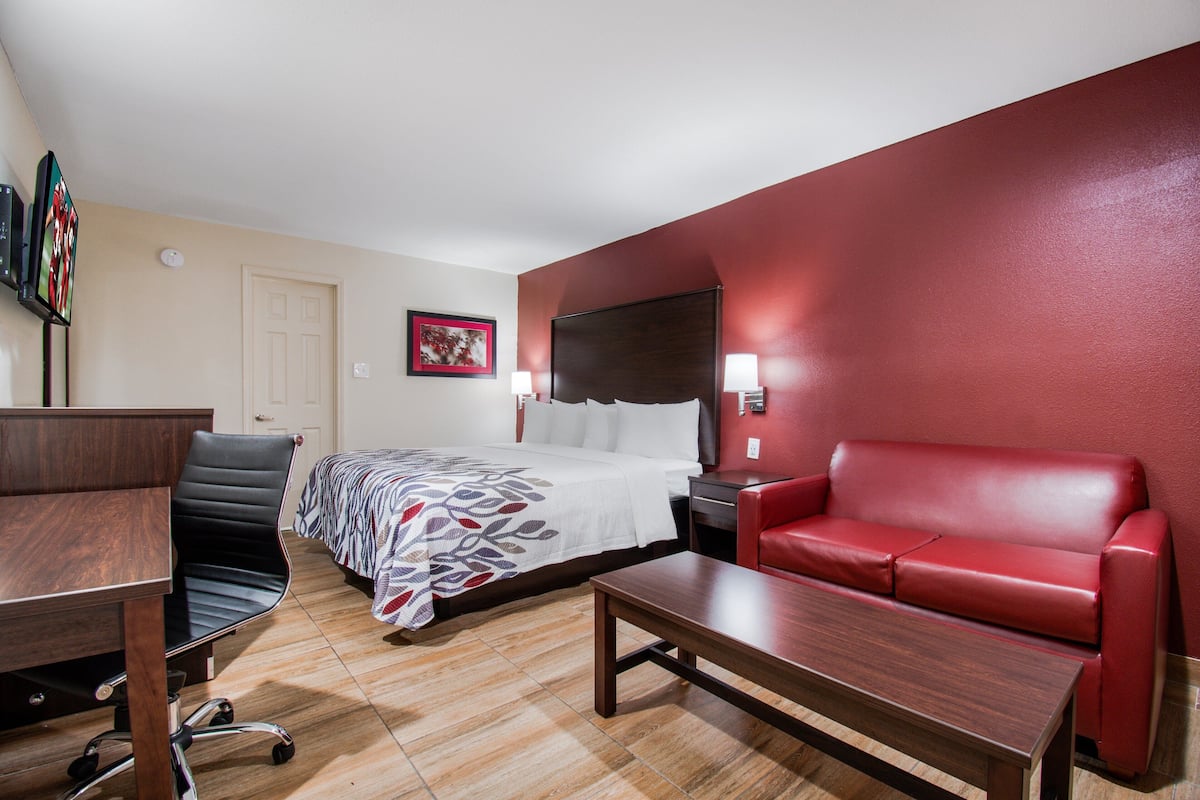 A hotel room with a bed, a red leather sofa, a wooden desk, and a chair.