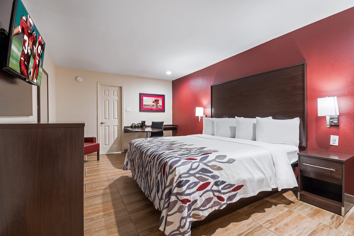 A hotel room with a large bed, a desk, a chair, and a TV on the wall.