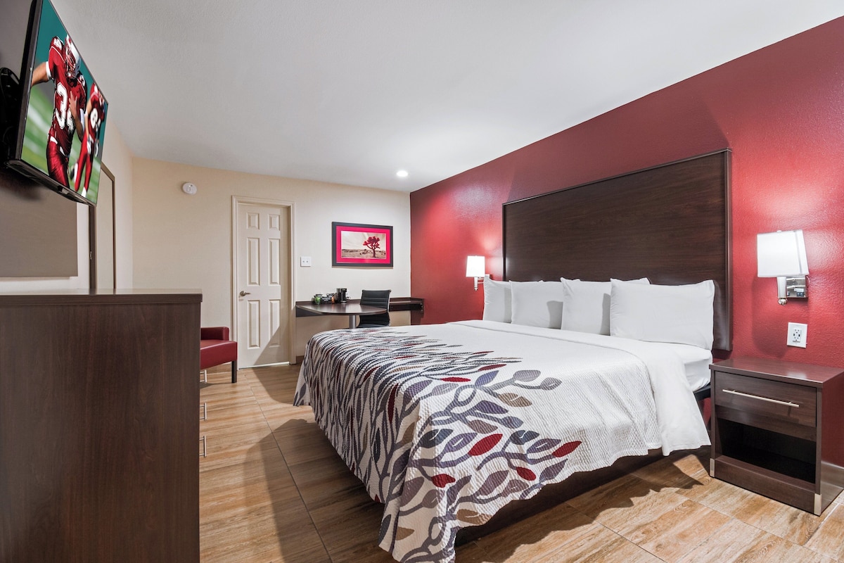 A hotel room with a bed, bedside tables, a desk, and a television.
