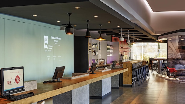 A modern bar area with a long counter, bar stools, and a projection screen displaying information. - Ibis Los Mochis (Los Mochis)