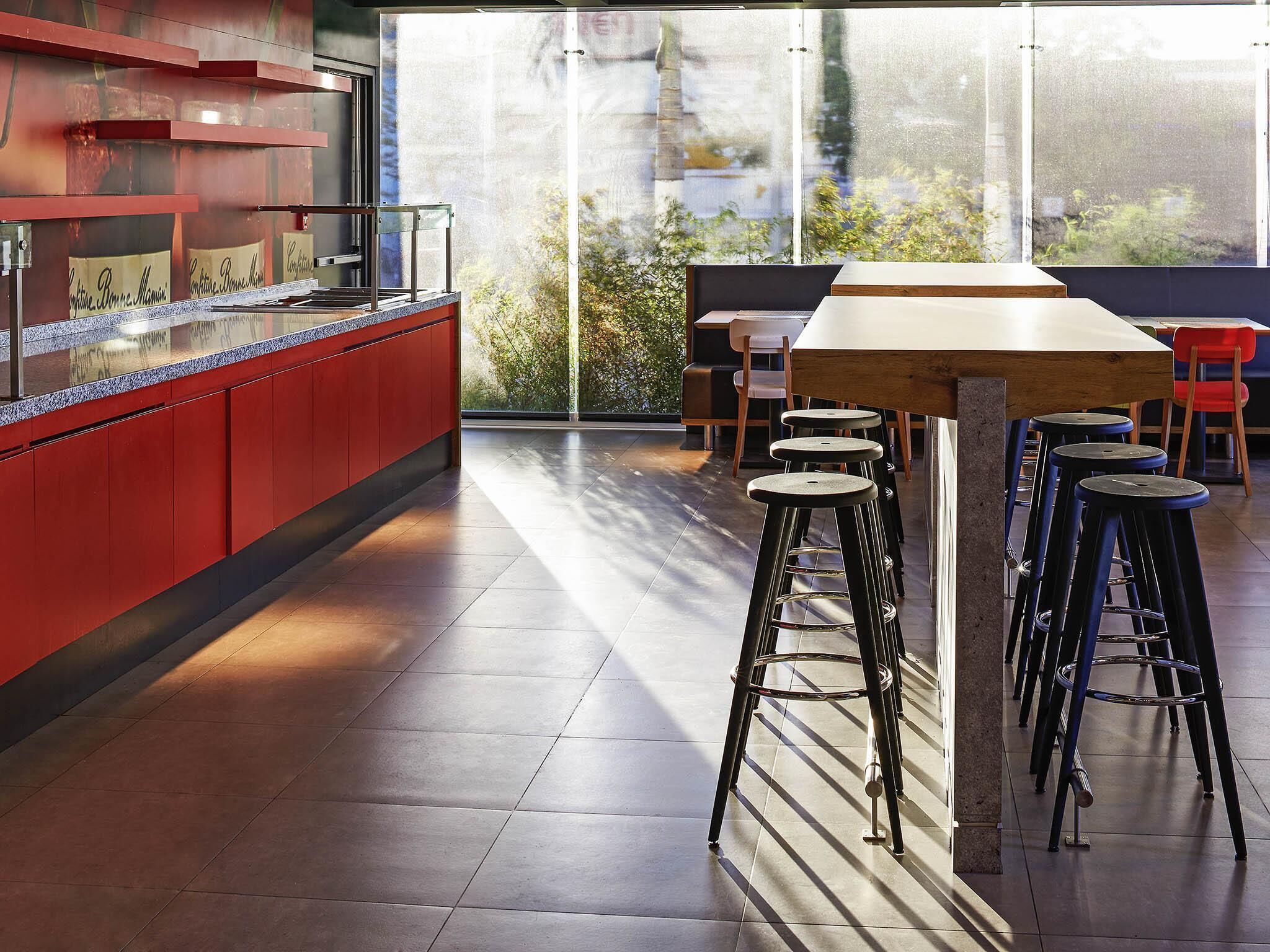 A modern bar area with stools, a counter, and a view of greenery outside.