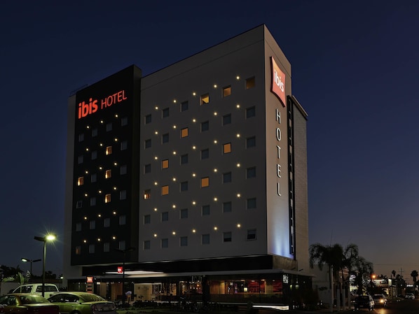Un hotel de varios pisos con ventanas iluminadas y un llamativo letrero de 'ibis'.