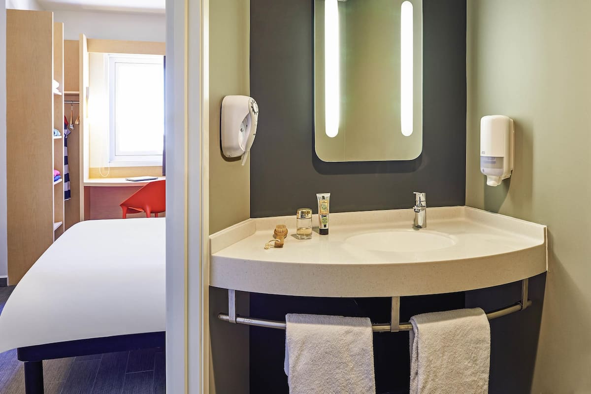 Ein Hotelbad mit einem großen Waschbecken, zwei Handtuchhaltern, einem Spiegel und einer Seifenspender.