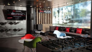 A modern lounge area with a foosball table, comfortable seating, a large TV screen, and a view through the window. - Ibis Los Mochis (Los Mochis)