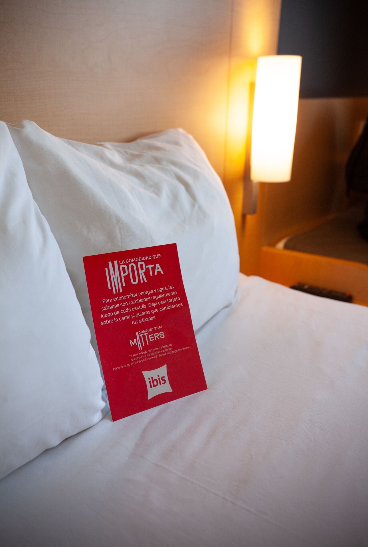 A hotel bed with a white pillow and a red informational card about energy and water conservation.
