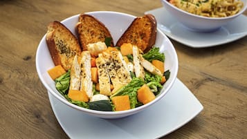 Un tazón blanco con ensalada, que incluye lechuga, pollo y queso, sobre una mesa de madera.