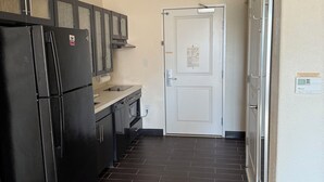 Una cocina compacta con piso oscuro, un refrigerador negro y una puerta blanca.