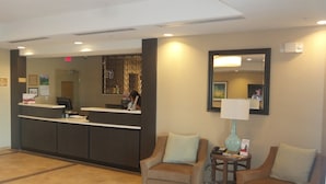 A reception area with a counter, two armchairs, a lamp, and a mirror on the wall. - Candlewood Suites Cotulla by IHG (Cotulla)