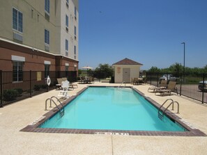 Piscina rectangular con un letrero de prohibición de clavados, rodeada por una cerca, y contigua a un edificio con señal de acceso para sillas de ruedas.