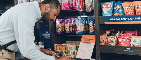 A person at a checkout counter in a store, with various snack items and a sign indicating a price of $1.50.