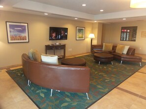 A hotel lobby with a brown leather sofa, a small table with a lamp, and a television on the wall. - Candlewood Suites Cotulla by IHG (Cotulla)