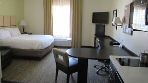 Habitación de hotel con cama, escritorio, silla, televisor y kitchenette.