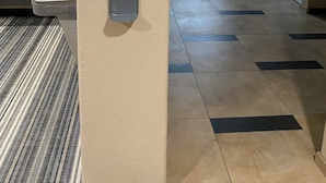 A gym area with a hand sanitizer dispenser, a sign with safety guidelines, and a window with blinds. - Candlewood Suites Cotulla by IHG (Cotulla)
