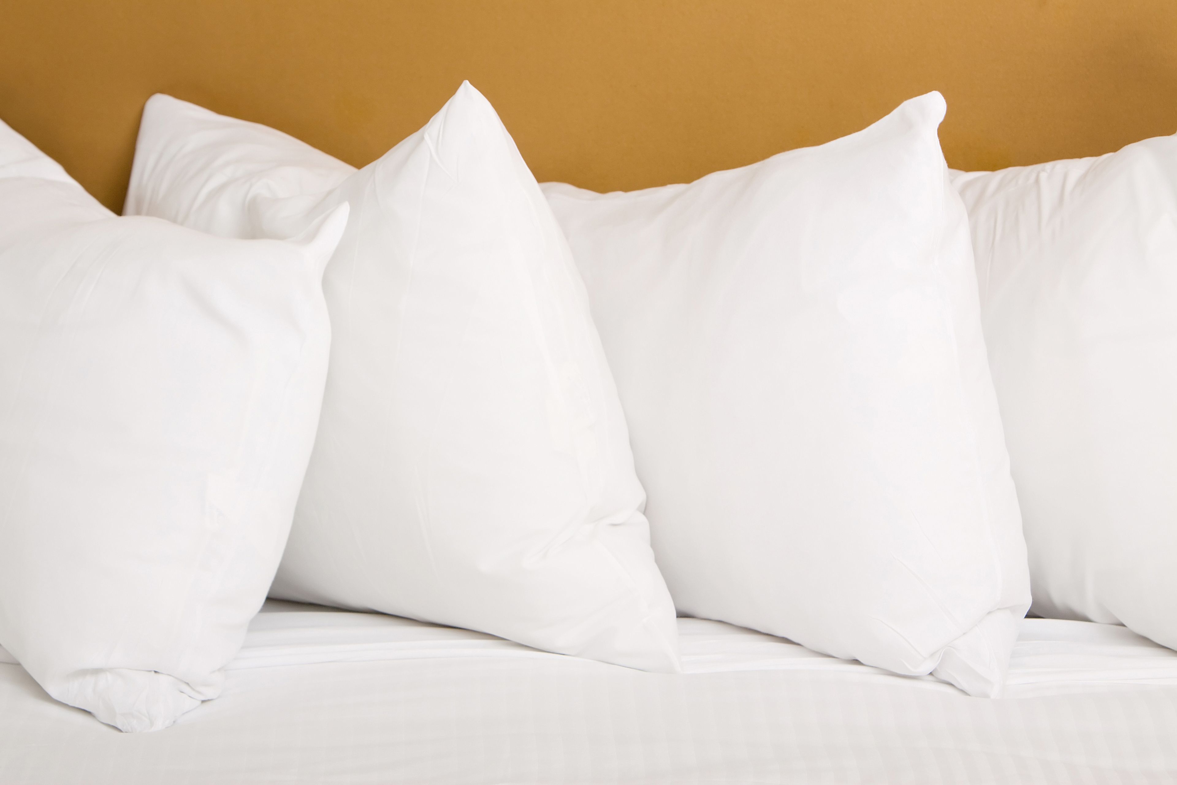 A bed with white bedding and pillows against a beige wall.
