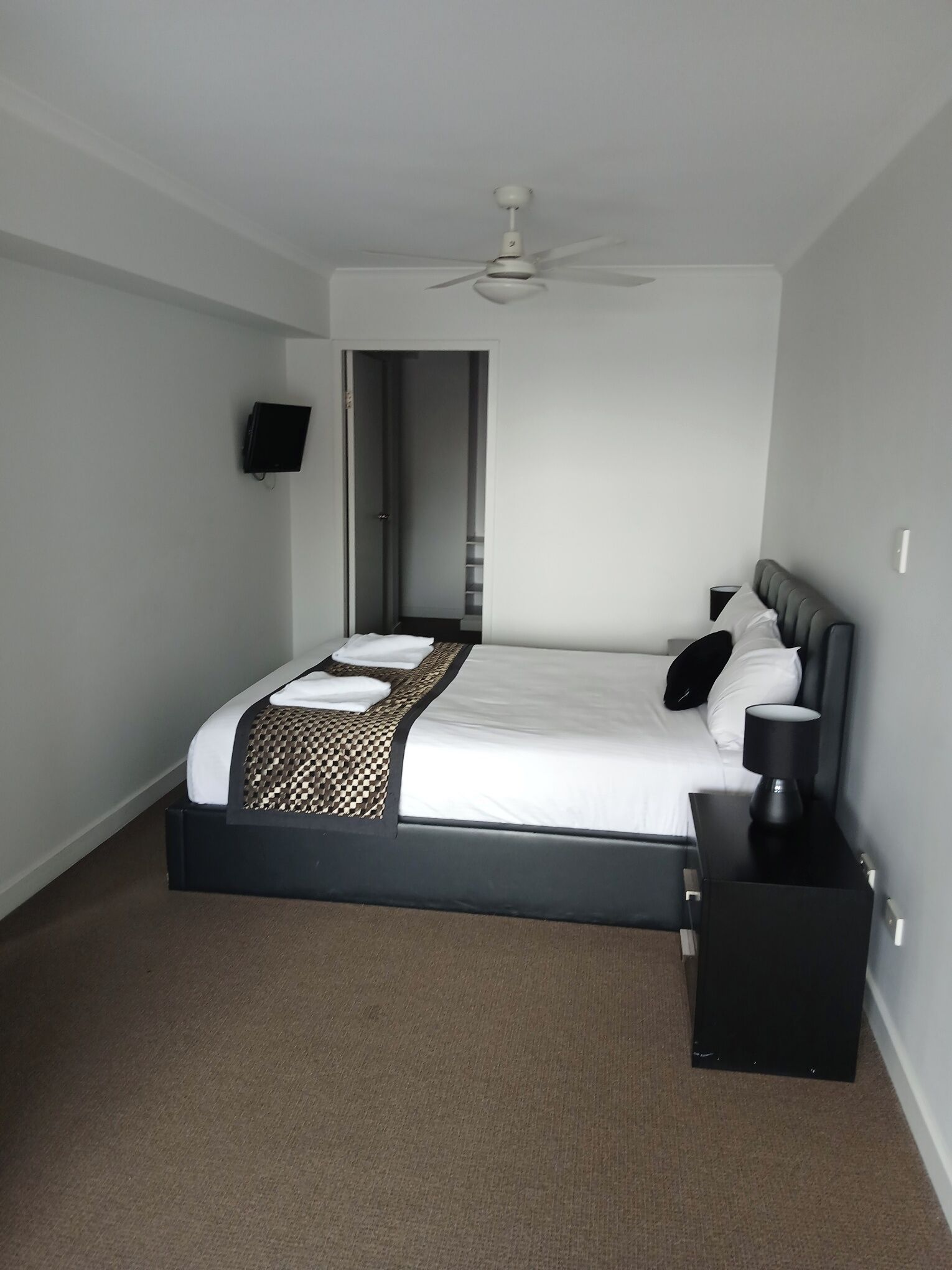 Ein Schlafzimmer mit einem Bett, einem Nachttisch, einem Deckenventilator und einem Fernseher an der Wand.