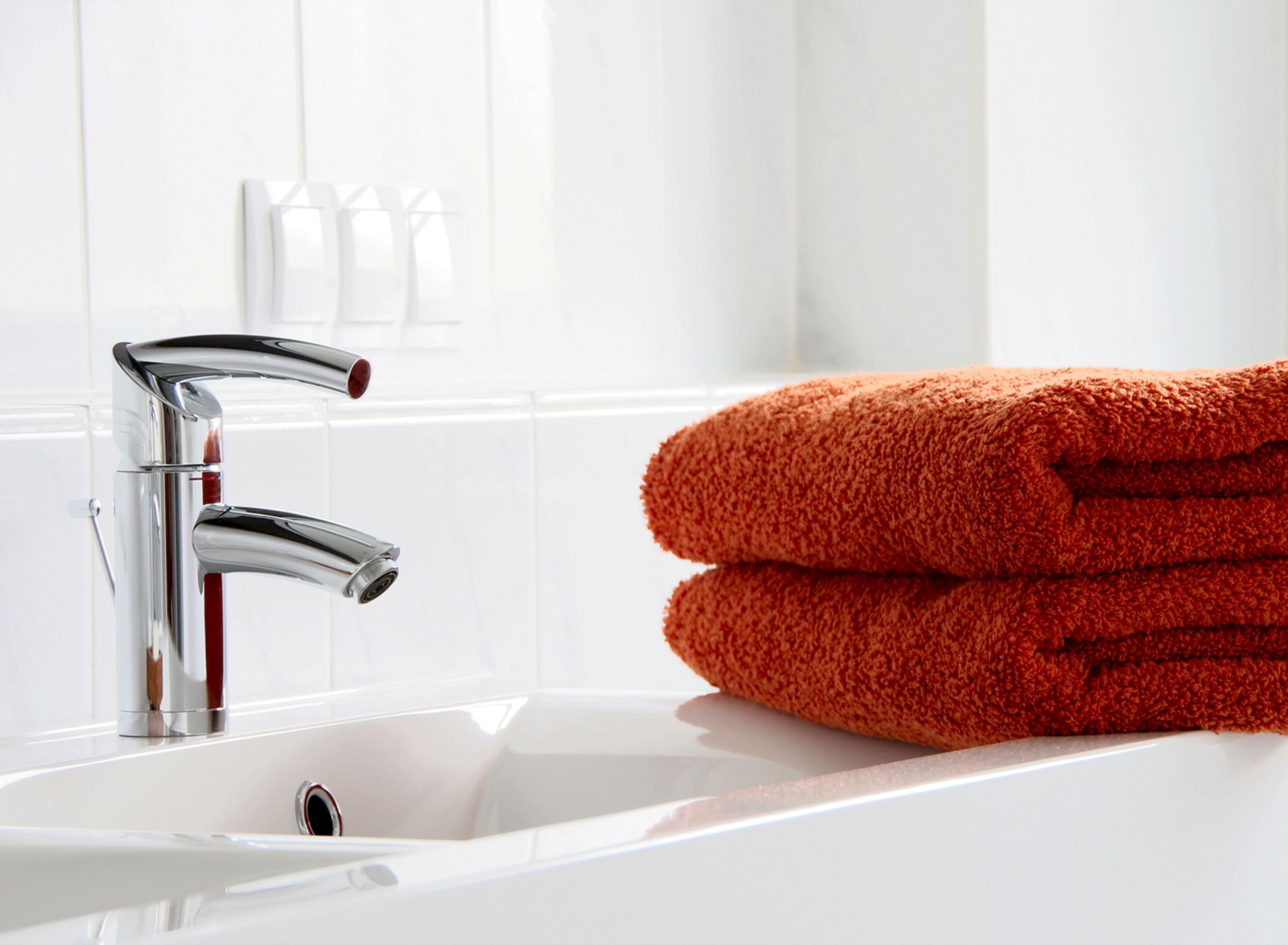 Ein Badezimmer mit einem chromfarbenen Wasserhahn, einem weißen Waschbecken und einem Stapel orangefarbener Handtücher.