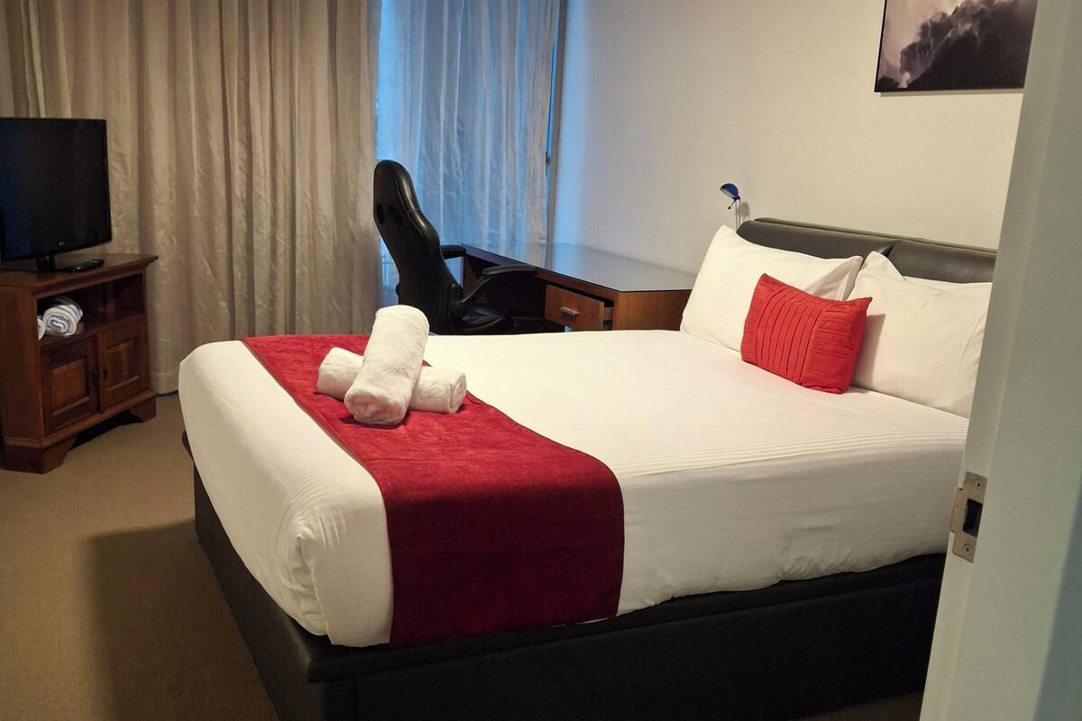 Ein Hotelzimmer mit Bett, Schreibtisch, Stuhl, Fernseher und Deckenventilator.